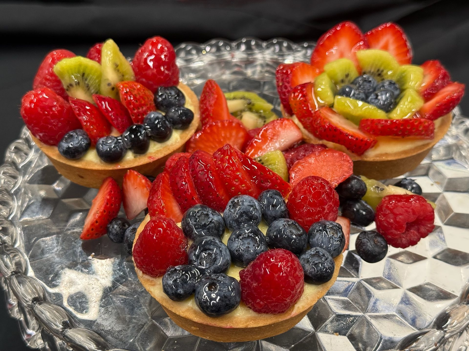 Fruit tarts with strawberries, blueberries, kiwi, and raspberries on a decorative glass plate.