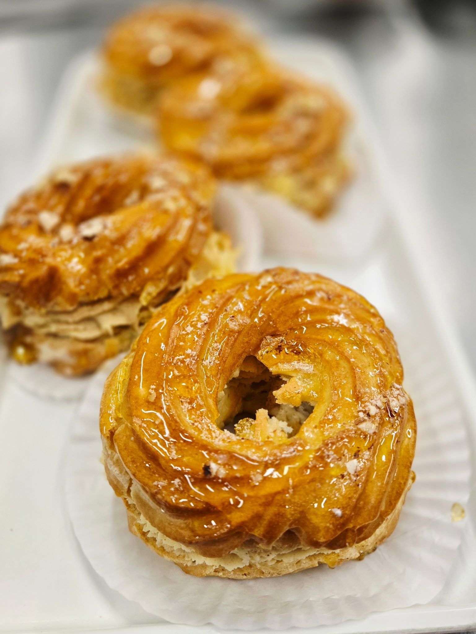 Close-up of glazed, ring-shaped pastries on a white platter with paper liners.
