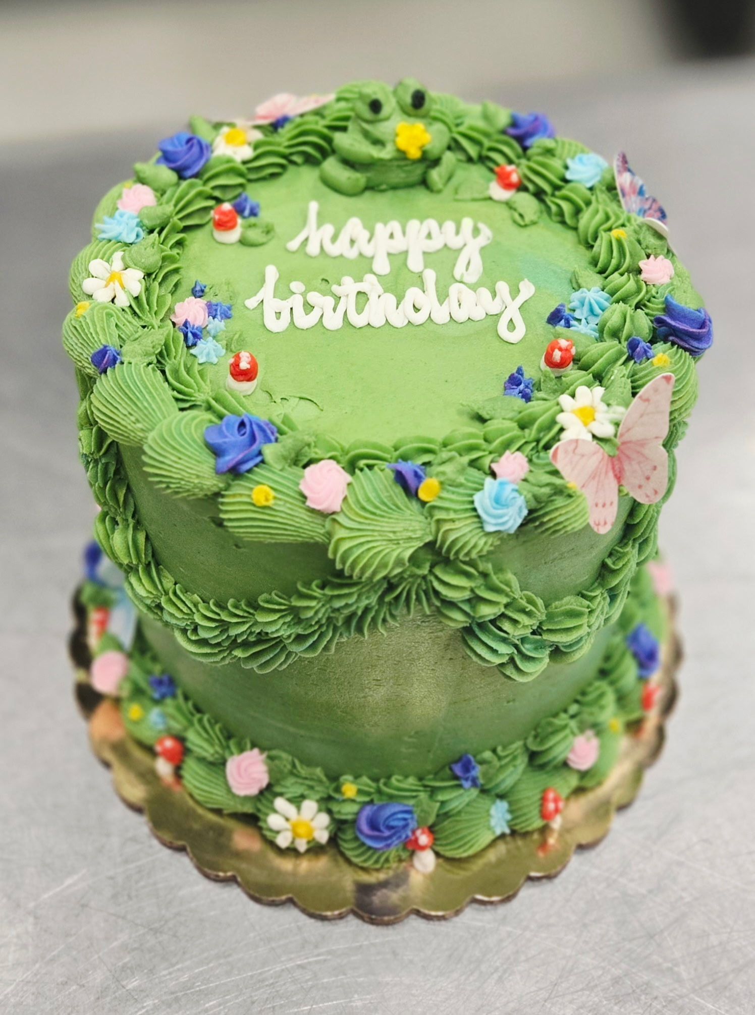 Green frosted birthday cake decorated with frosting vines, flowers, and a frog.