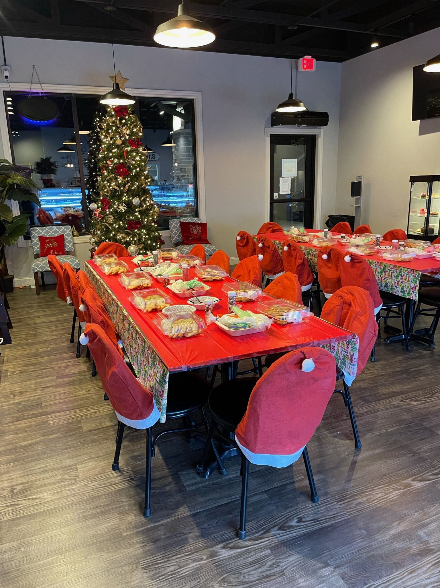 Christmas-themed dining room: red table settings, Santa hat chair covers, decorated tree, and overhead lights.
