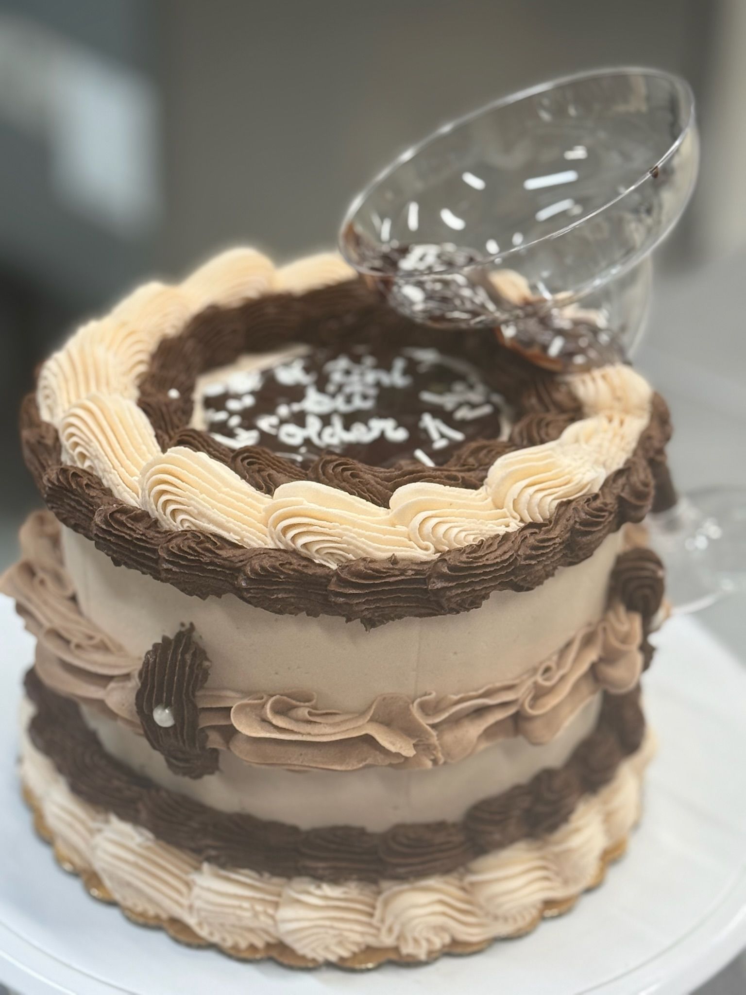Chocolate cake decorated with tan and brown frosting, topped with an overturned glass.