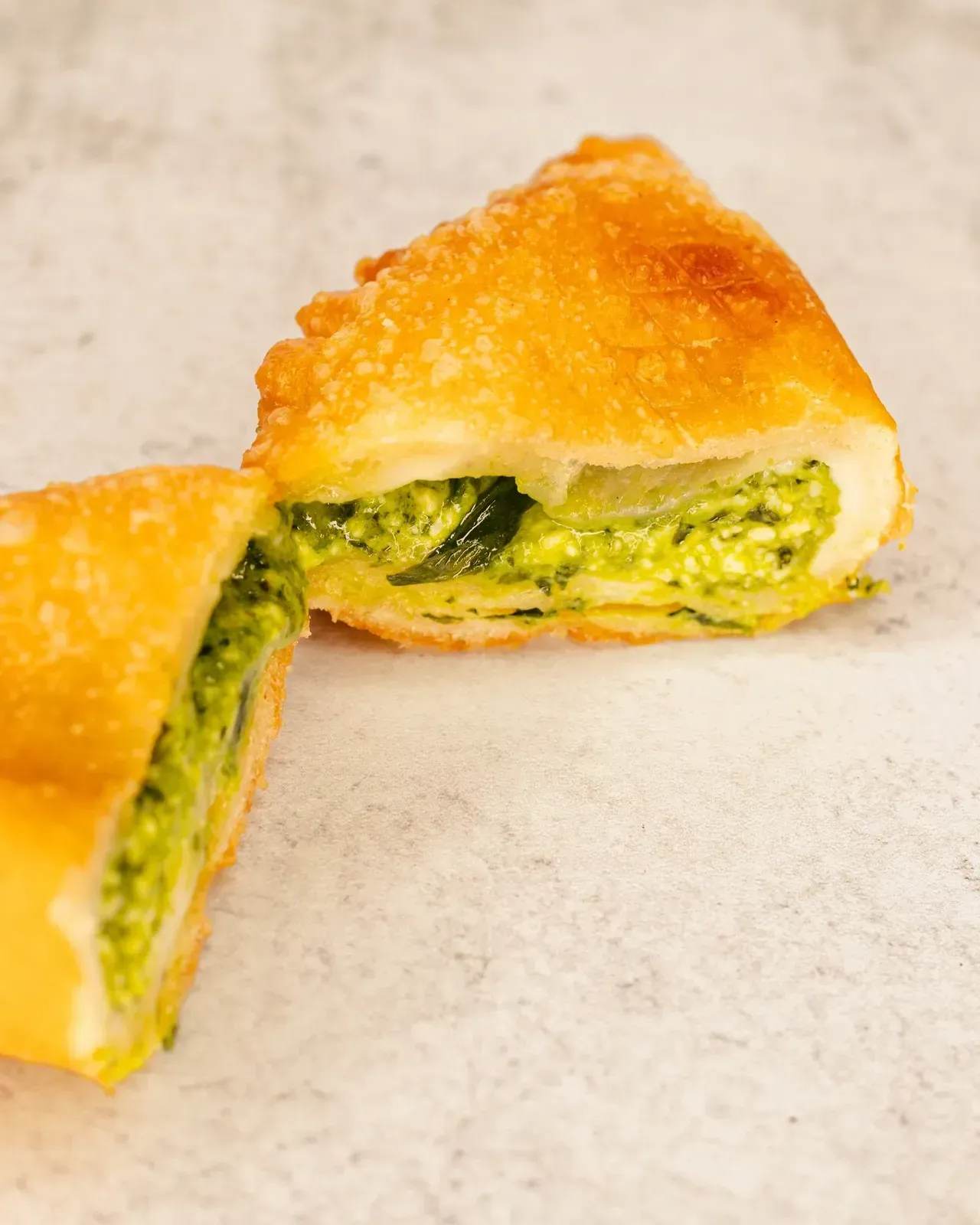 Deep-fried pastry filled with green pesto. One half cut open, showing the filling and golden crust.