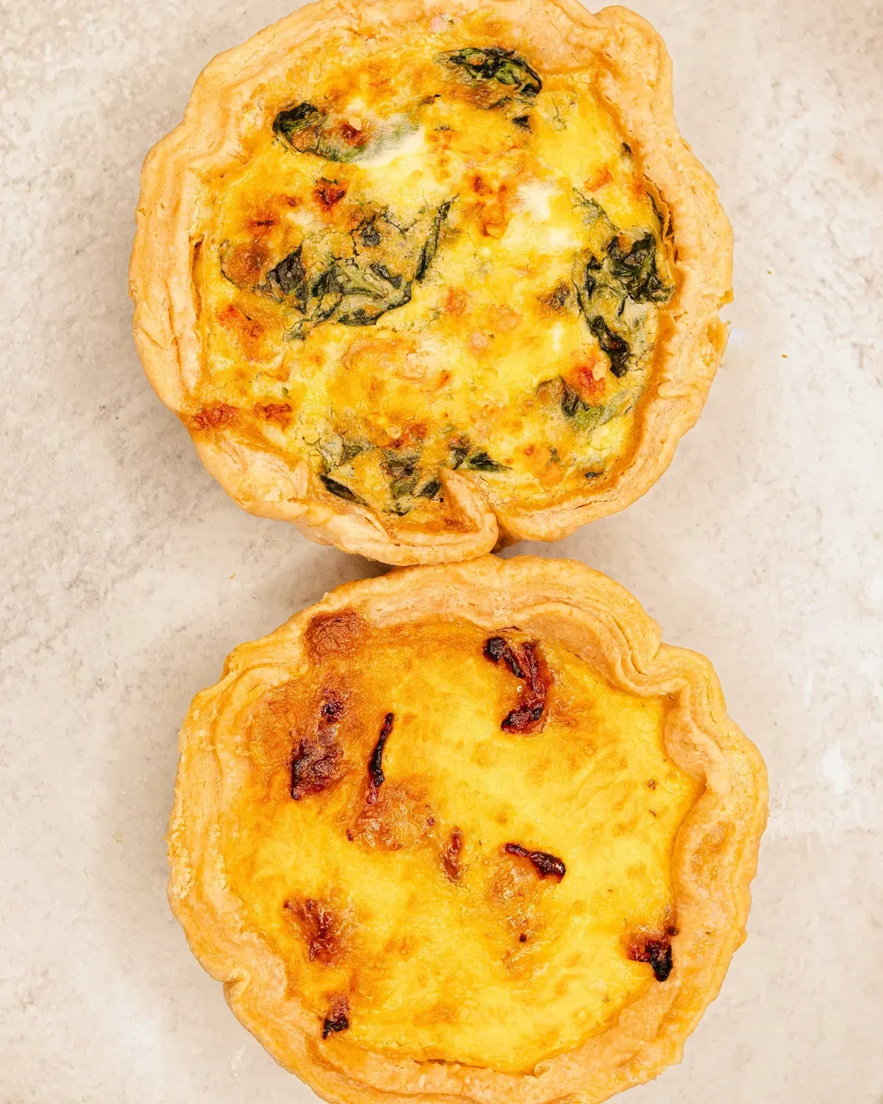Two quiches in flaky crusts, one with spinach, one with bacon.
