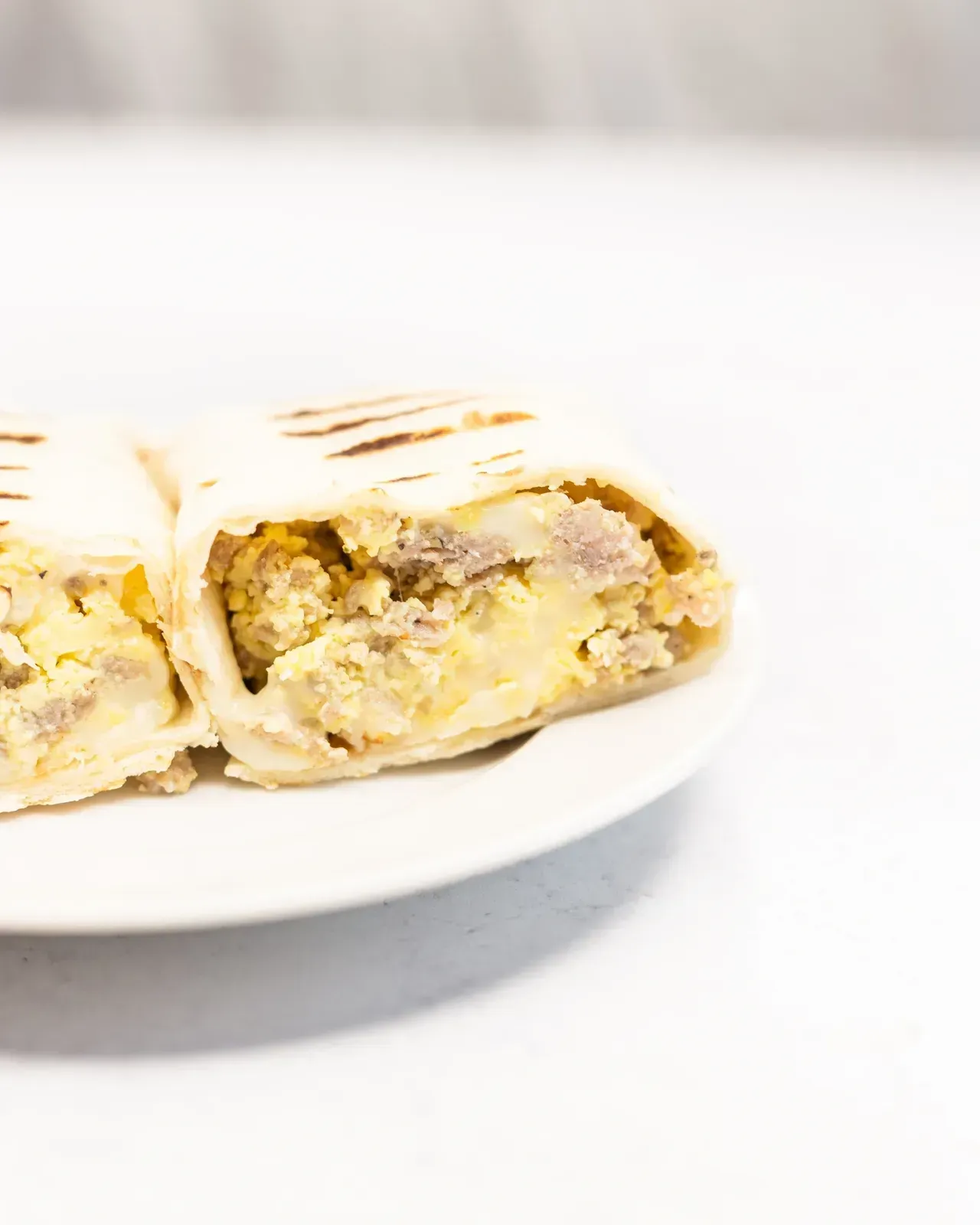 Breakfast burrito cut in half on a white plate, revealing egg and sausage filling.