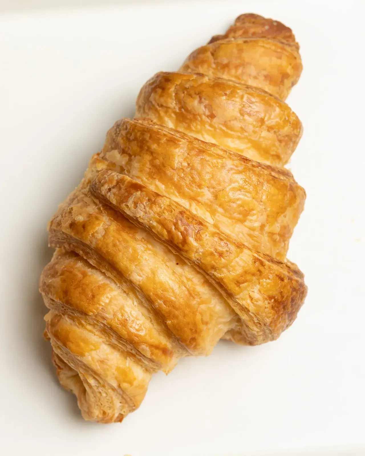 Golden-brown croissant, flaky layers, on a white surface.