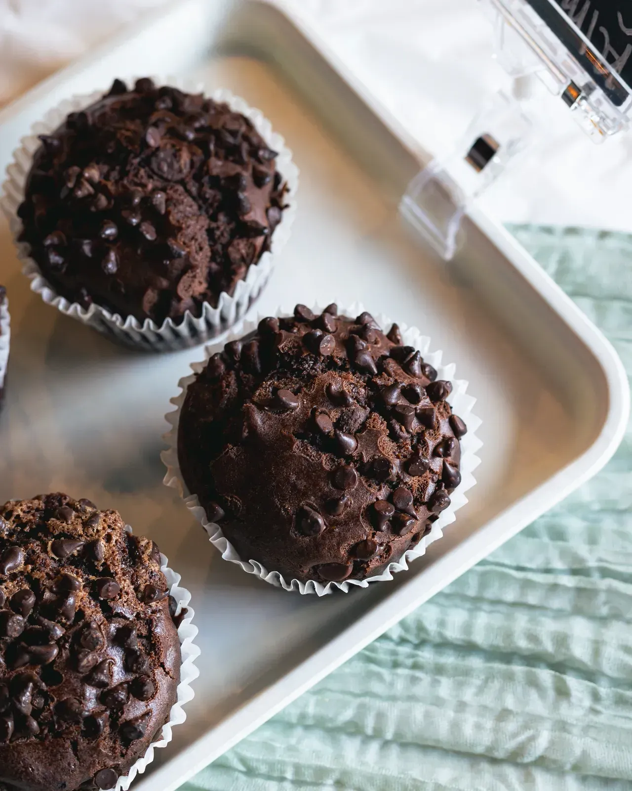 Chocolate chip muffins in white paper liners on a white tray.