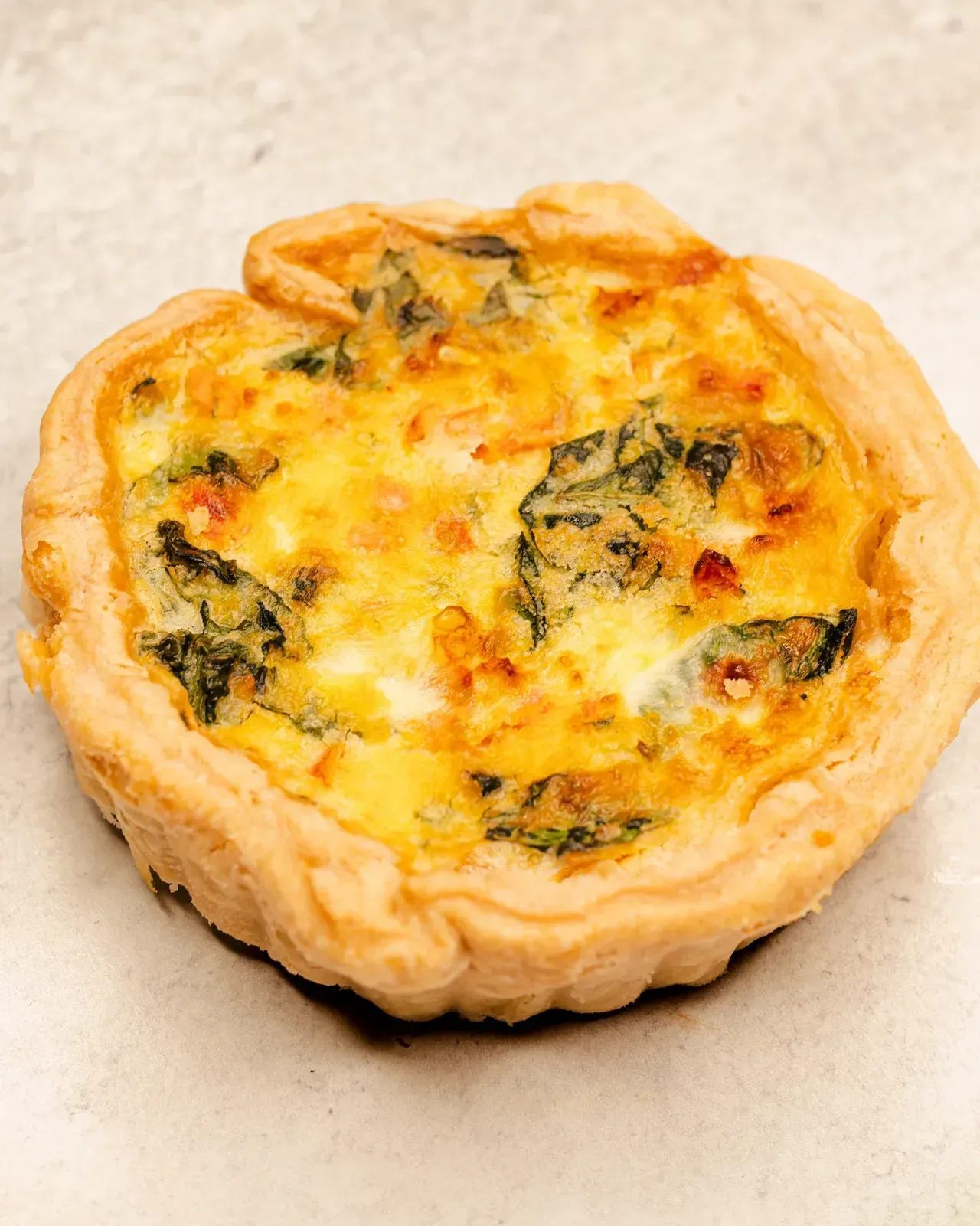 Small quiche with golden crust, filled with egg custard and visible spinach.