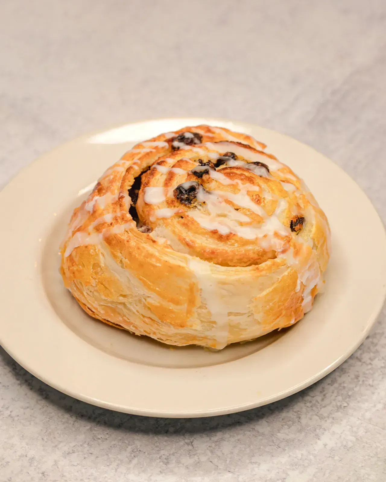 Cinnamon roll with icing on a beige plate.