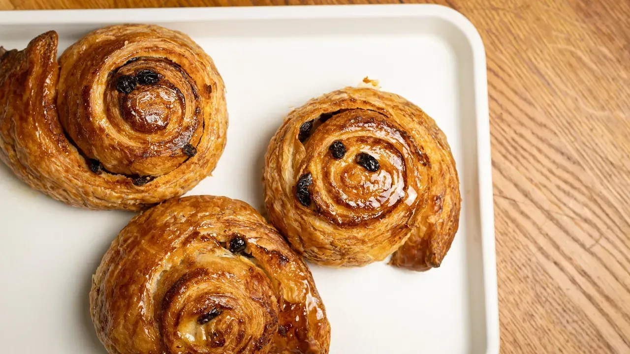 Three glazed cinnamon swirl pastries on a white tray, set on a wooden table.