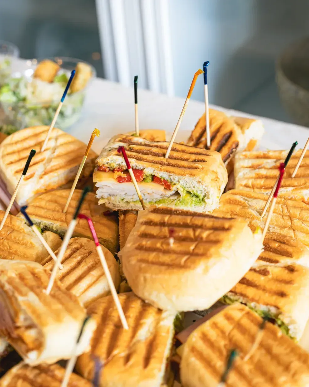 Panini sandwiches on a platter, cut into halves and secured with colorful toothpicks.