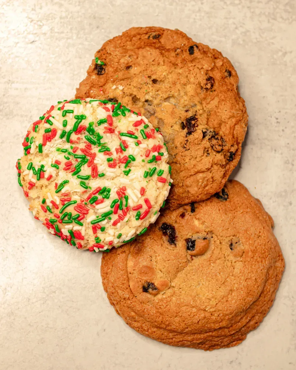 Three cookies: one with red and green sprinkles, two chocolate chip.
