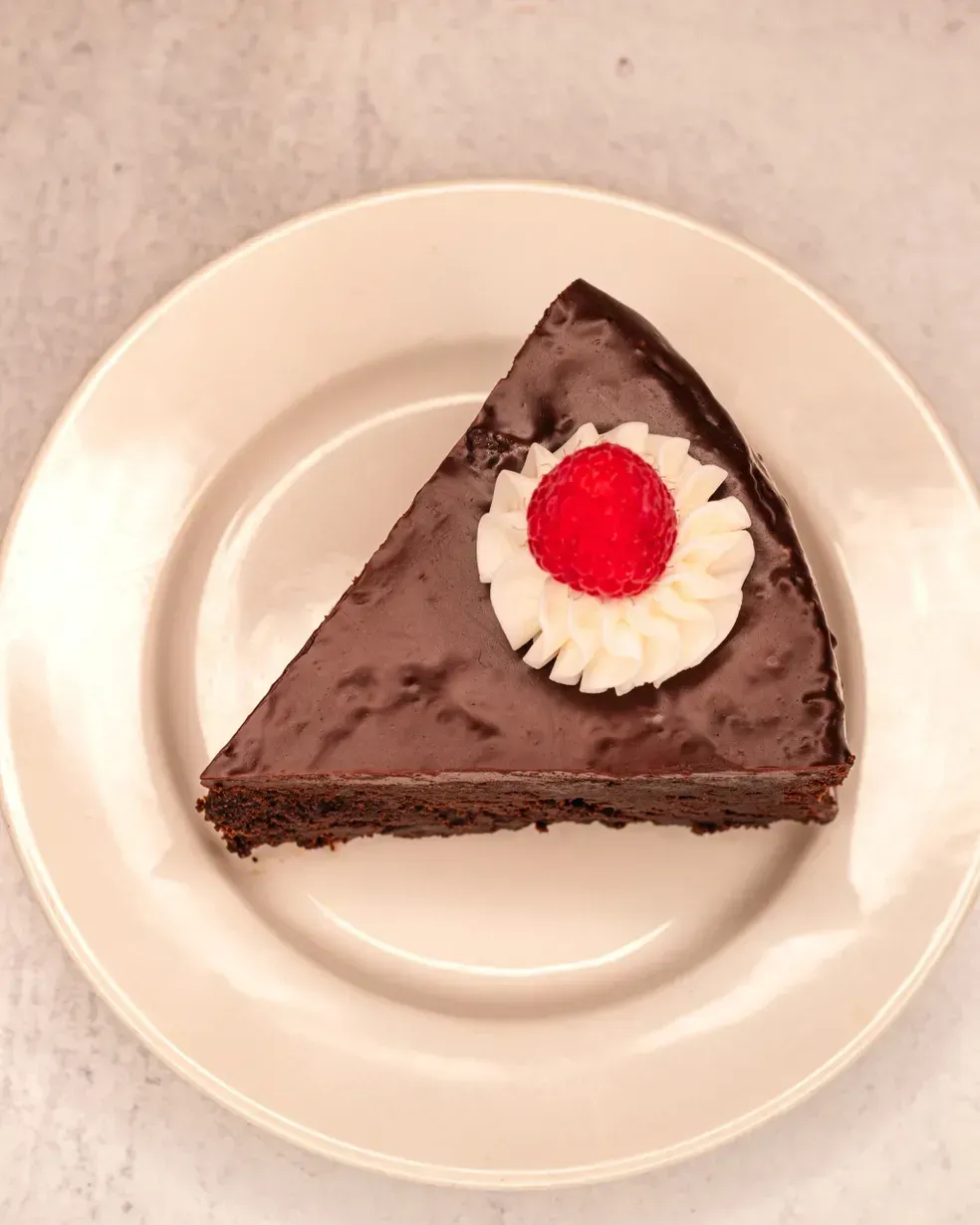 Slice of chocolate cake with white frosting and a cherry on a white plate.