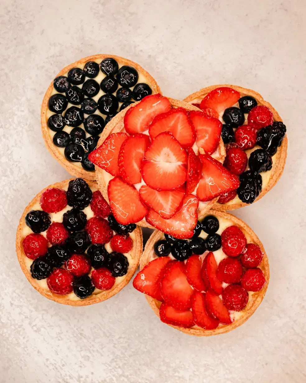 Fruit tarts with blueberries, strawberries, and raspberries, arranged on a light surface.