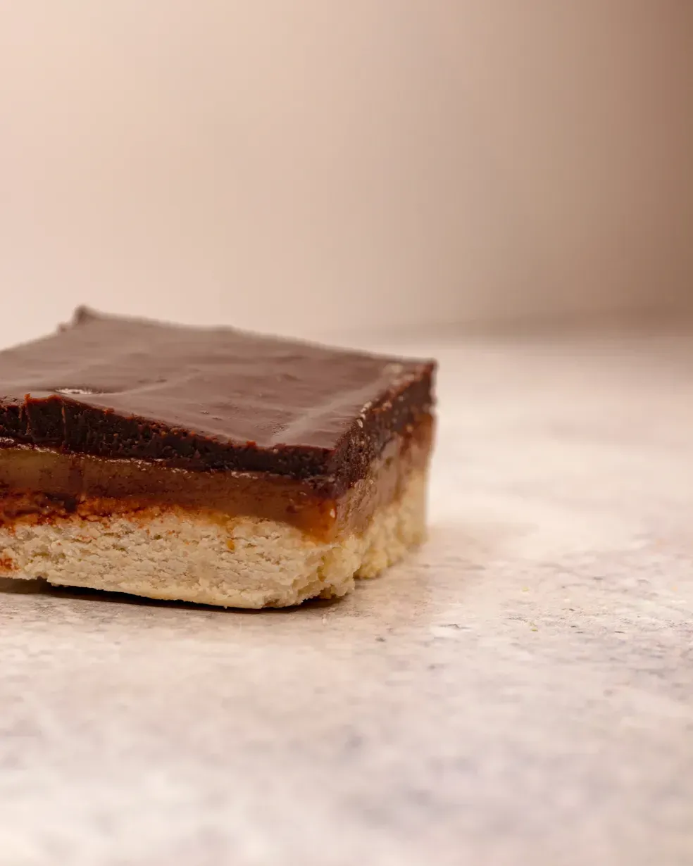 Chocolate caramel shortbread bar on a light surface.