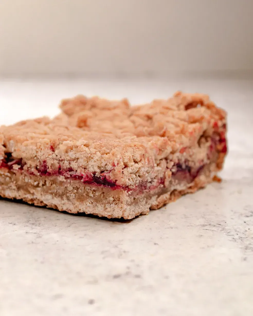 A square dessert with a crumb topping and a visible berry filling, on a white surface.