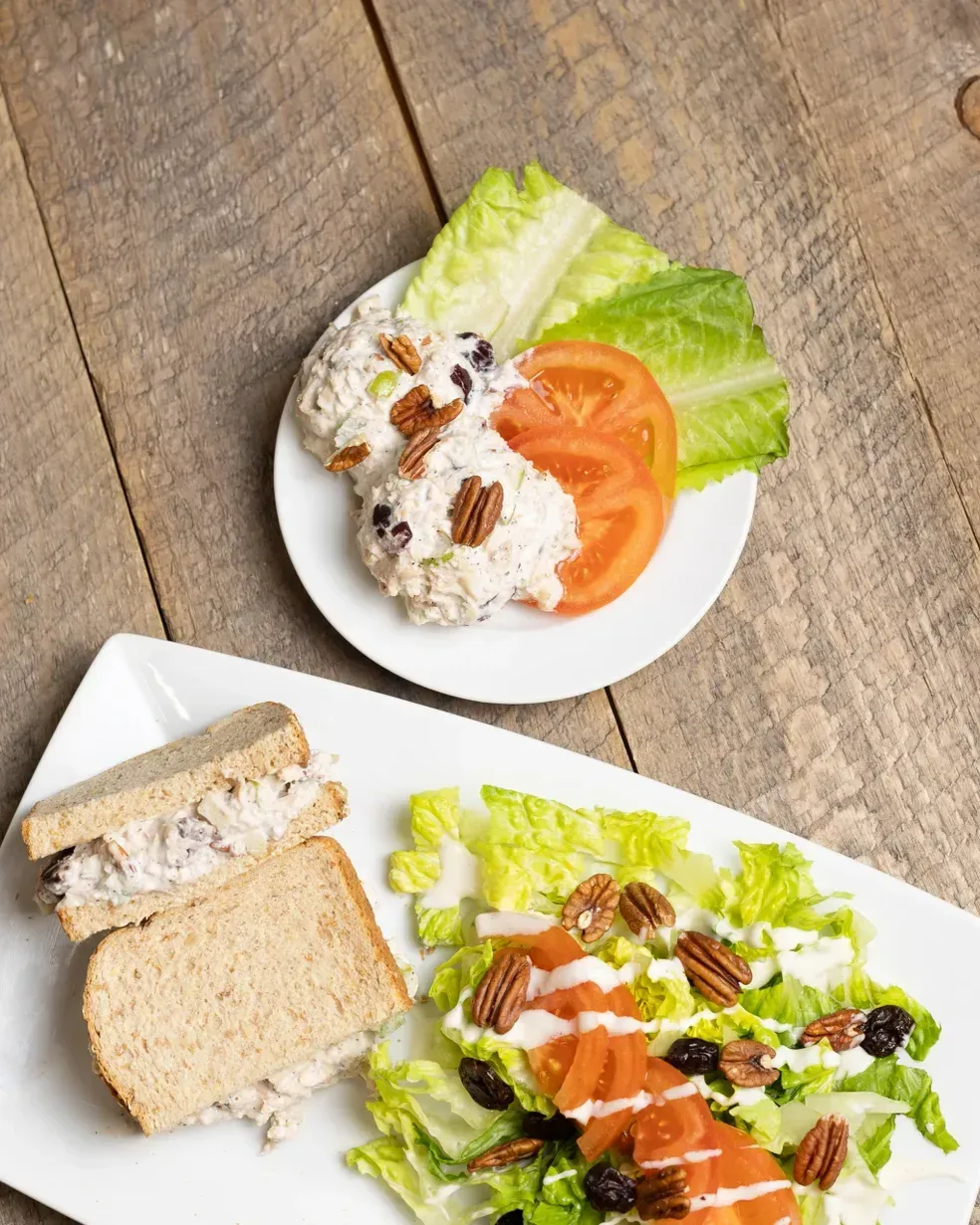 Chicken salad plate with sandwich and salad components on a wooden table.