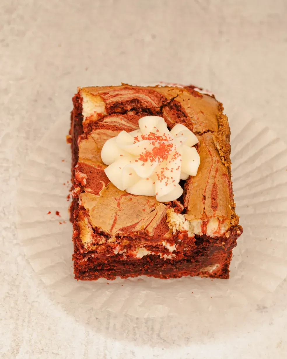 Red velvet brownie topped with white frosting and red sprinkles.
