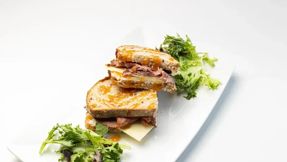 Grilled roast beef sandwich on white plate with salad.