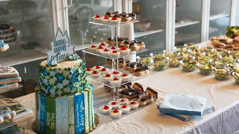 Dessert table with tiered cake, pastries, and cupcakes in a bright room.