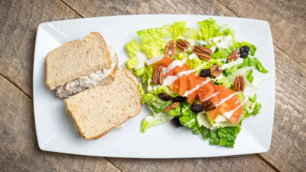 Sandwich and salad on a white plate, set on a wooden surface.