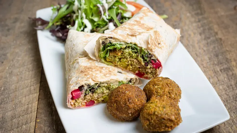 Falafel wrap cut open with falafel balls, salad, and white sauce on a white plate.