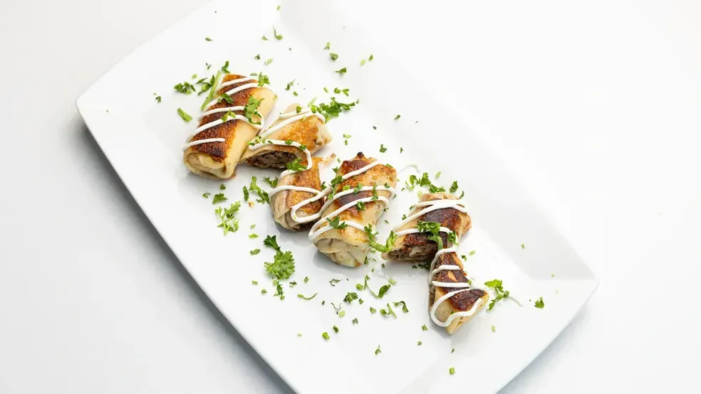 Appetizers arranged on a white plate, drizzled with white sauce and parsley.