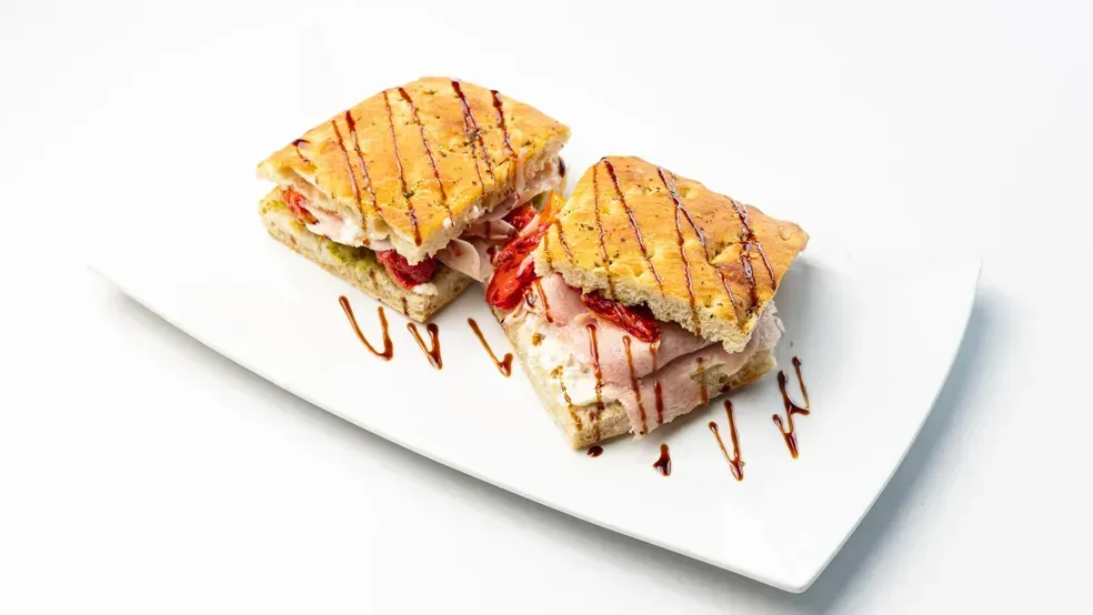 Two panini sandwiches on a white plate, drizzled with balsamic glaze.