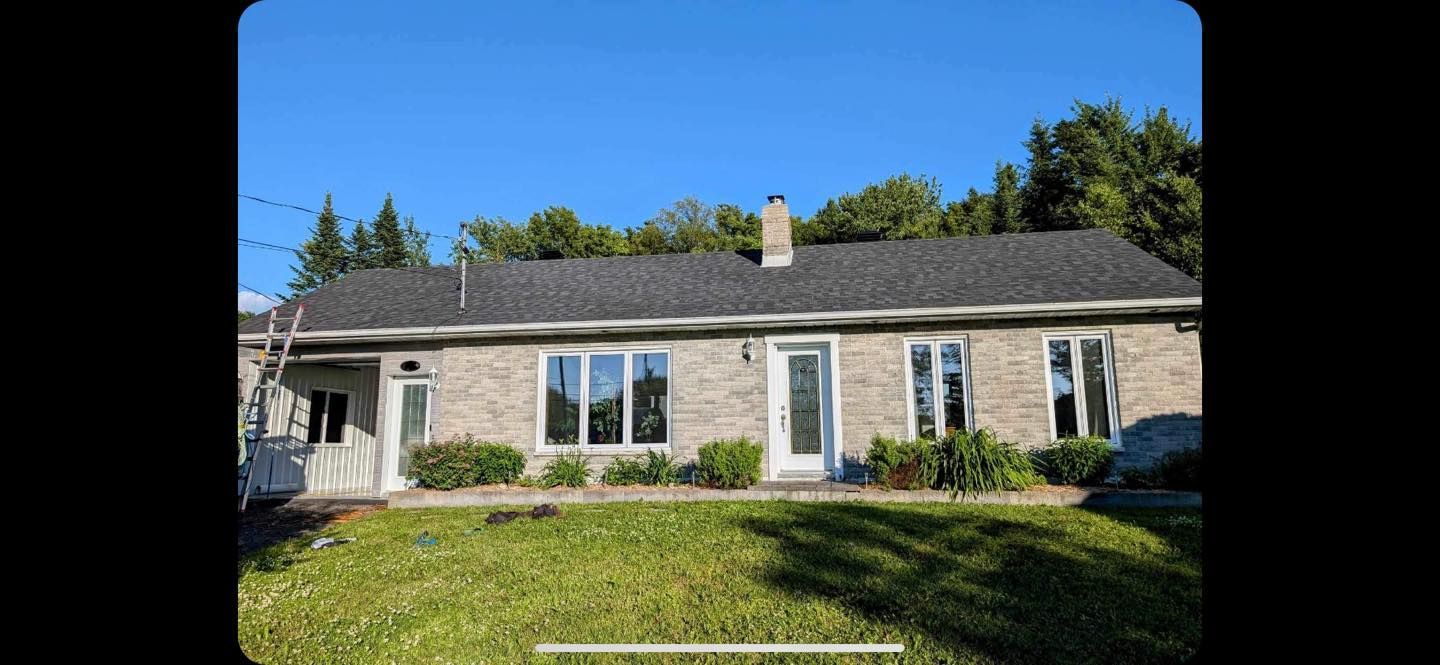 A brick house with a black roof is sitting on top of a lush green lawn.