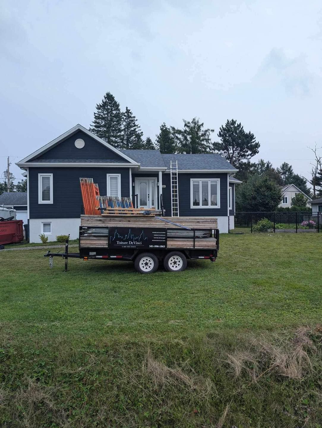A trailer is parked in front of a house in a grassy field.