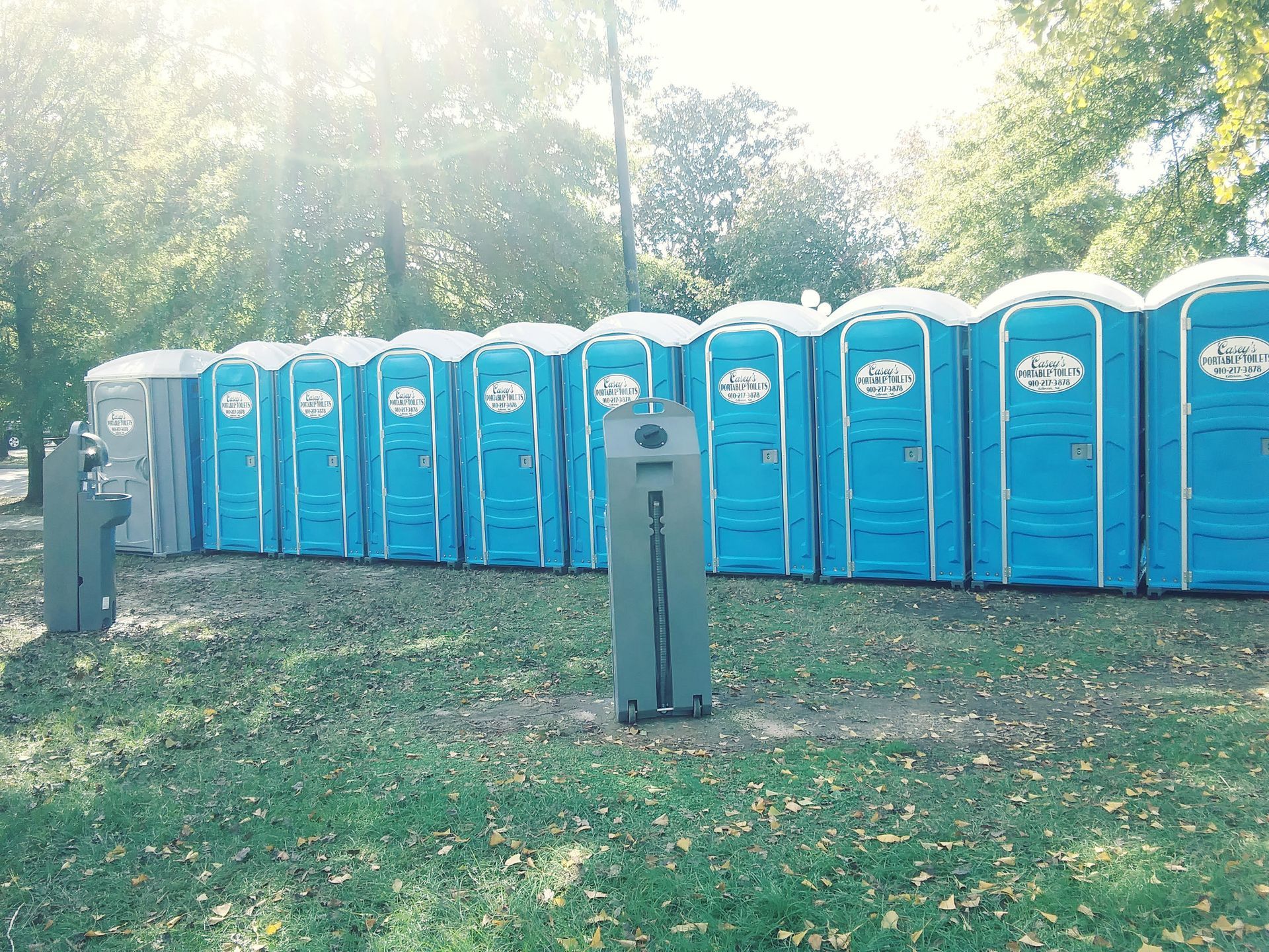 A row of portable toilets are lined up in a park.