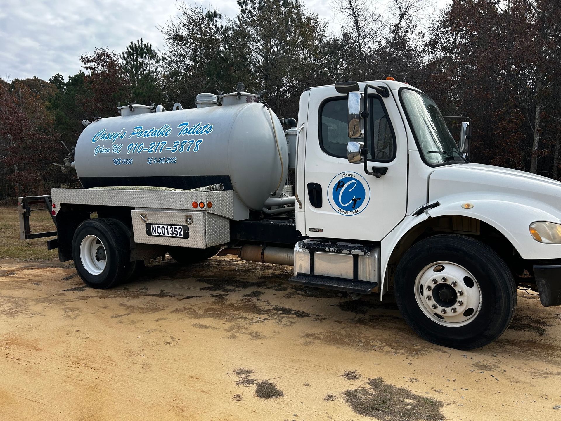 A white tanker truck is parked in a dirt field.