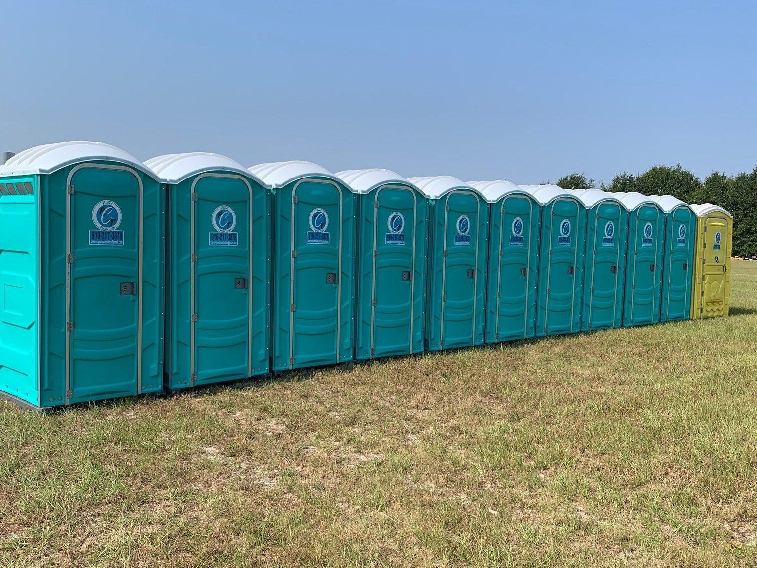 A row of portable toilets are lined up in a field.