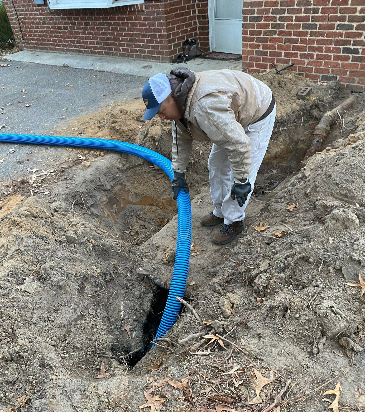 A man is digging a hole in the ground with a blue hose.