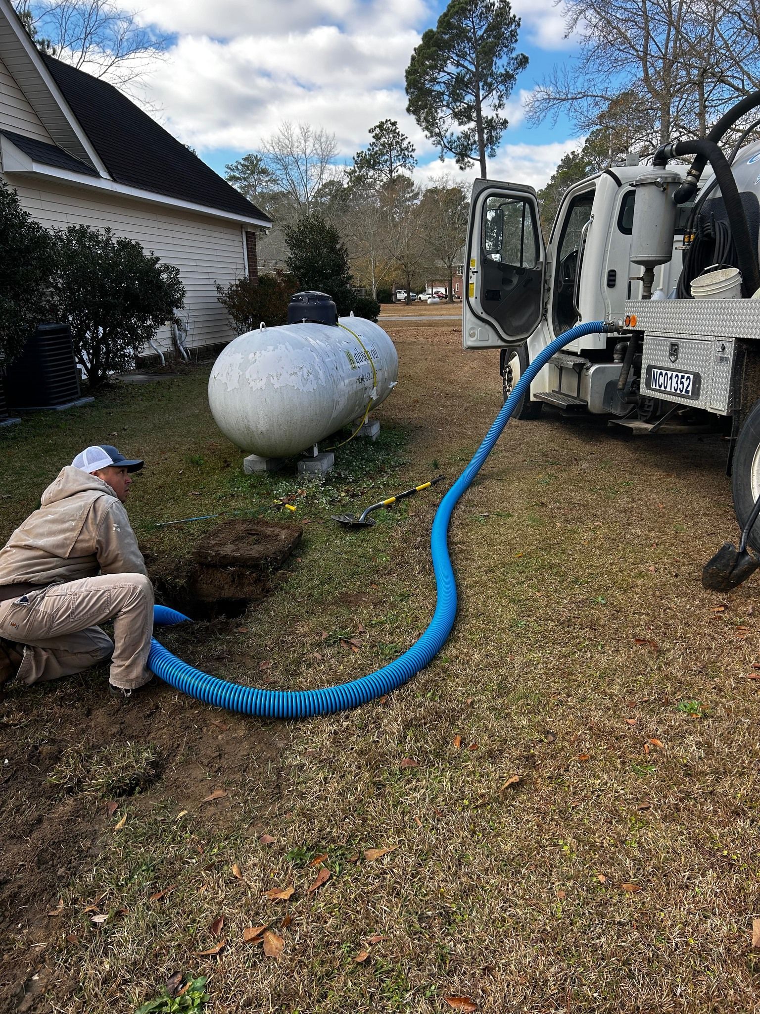 A man is kneeling in front of a septic tank being pumped by a truck.