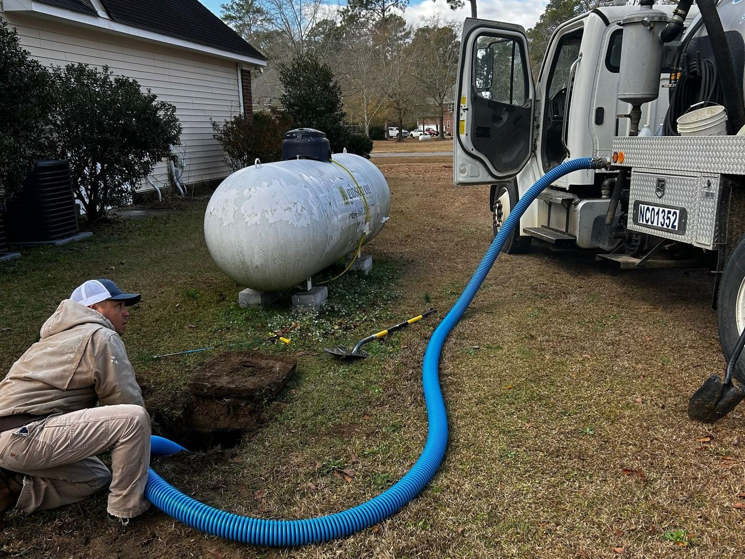 A man is kneeling in front of a propane tank next to a truck.