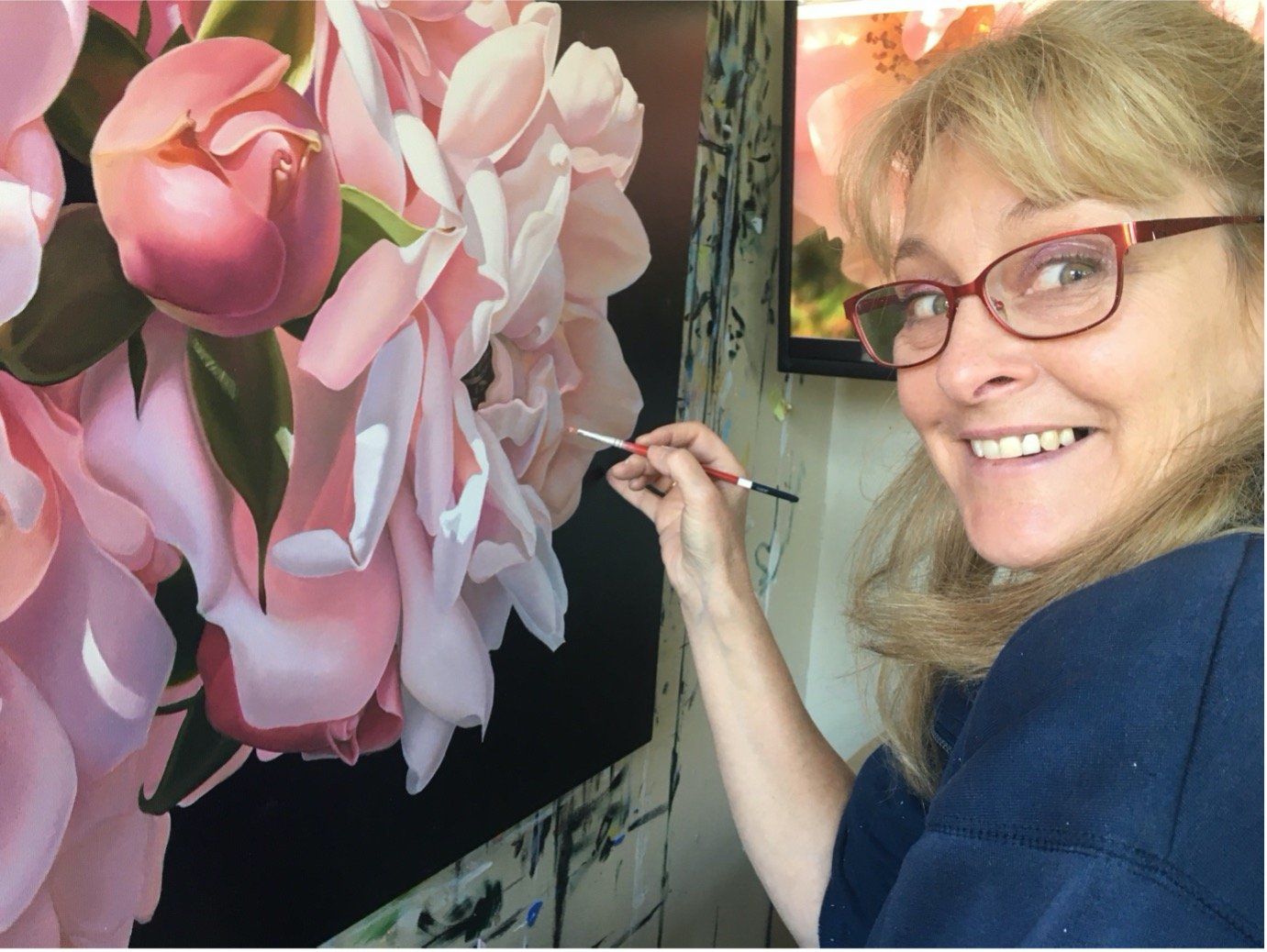 A woman wearing glasses is painting a picture of pink flowers.