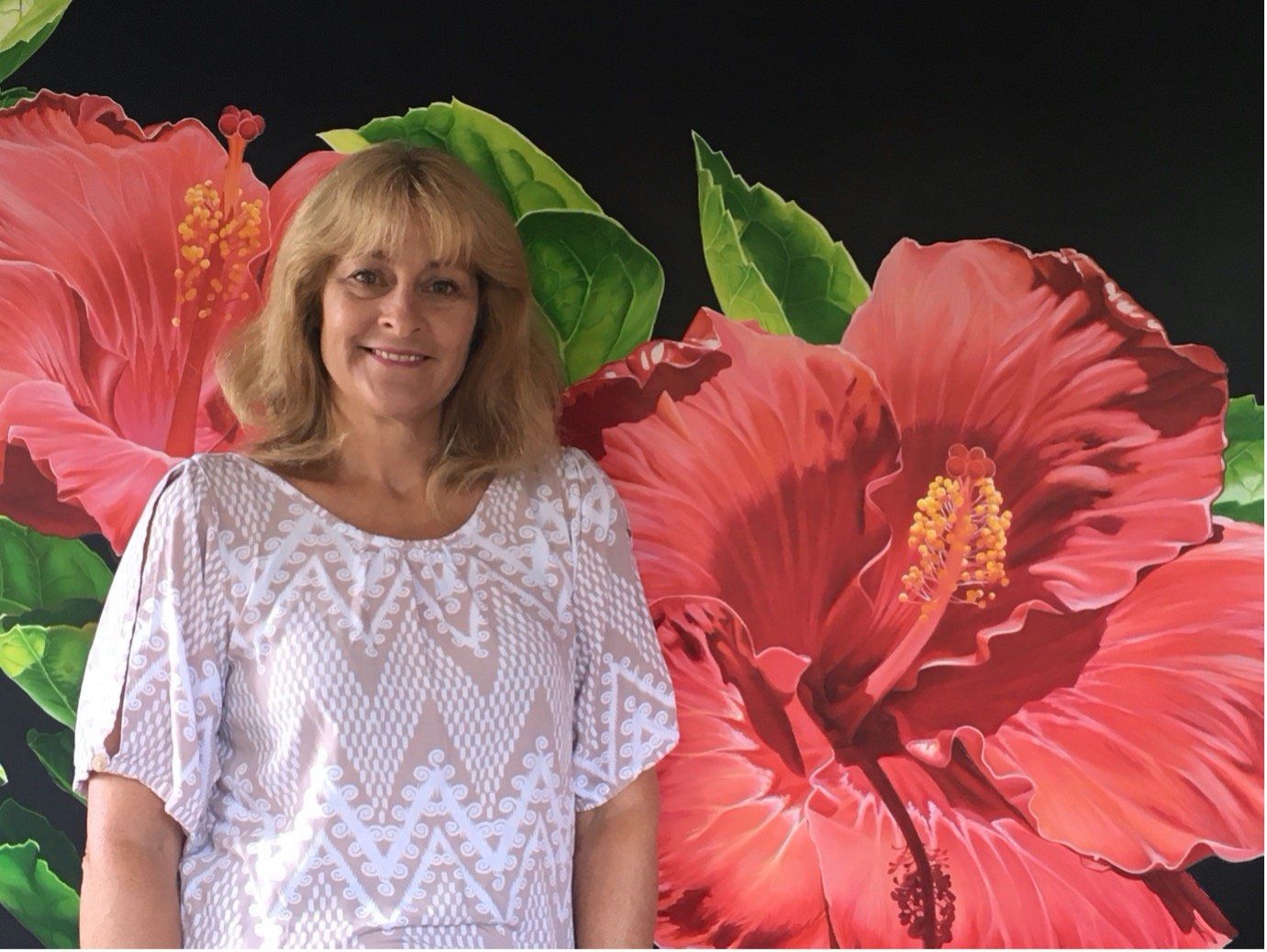 A woman is standing in front of a painting of red flowers.