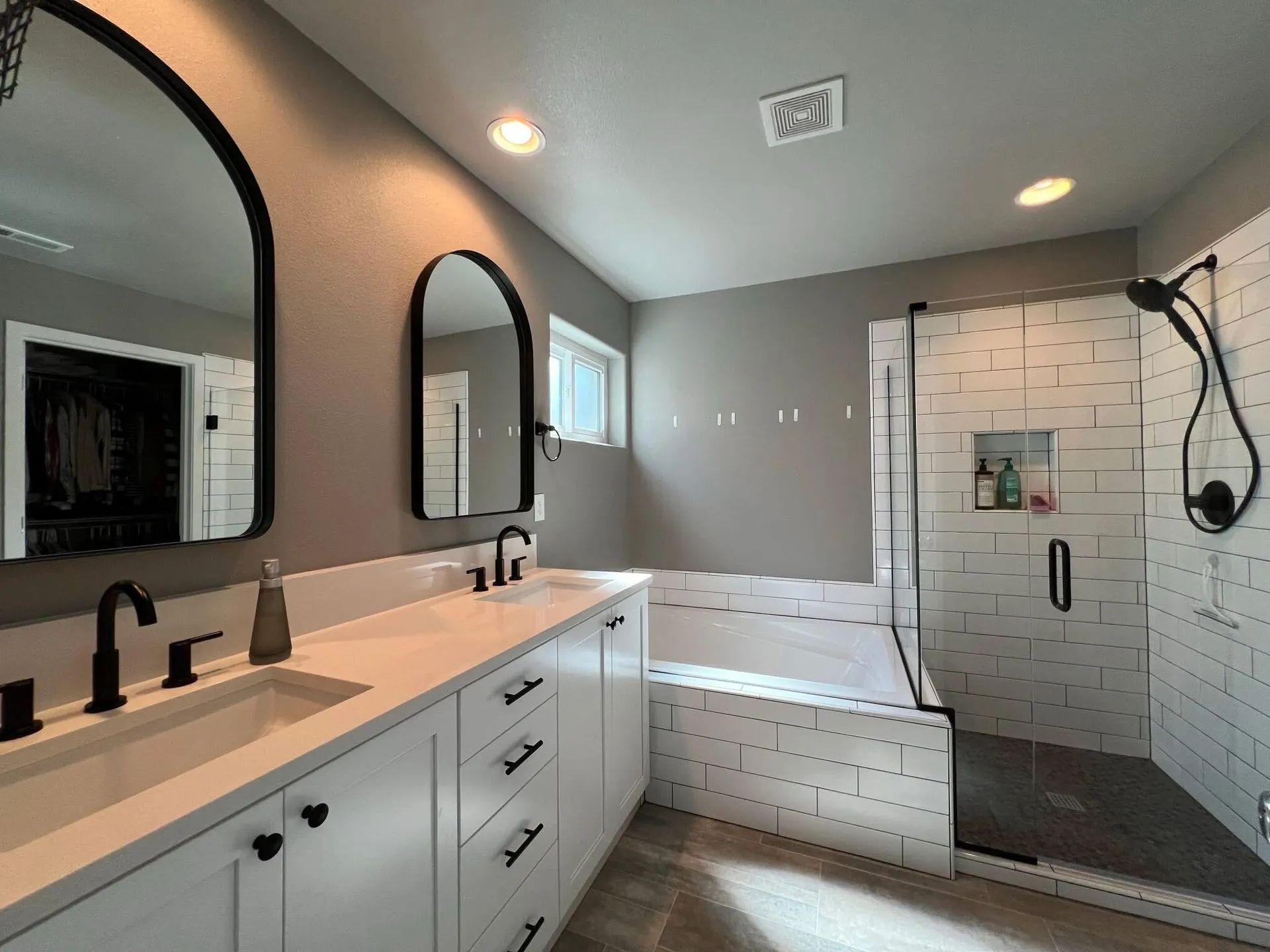 Modern bathroom with double vanity, arched mirrors, freestanding tub, and tiled walk-in shower