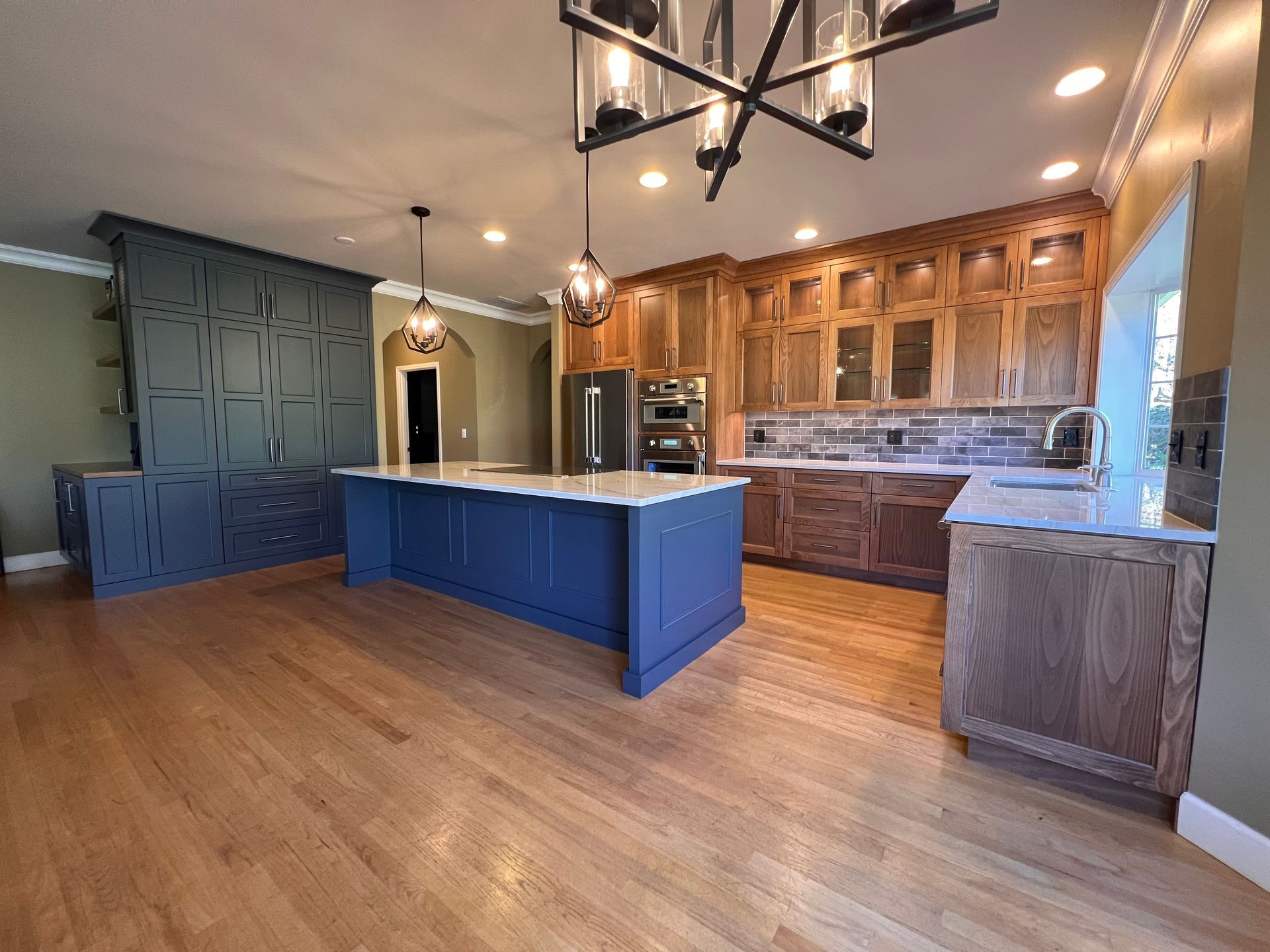 Spacious kitchen with blue island, wood floors, warm wood cabinets, and pendant lighting.