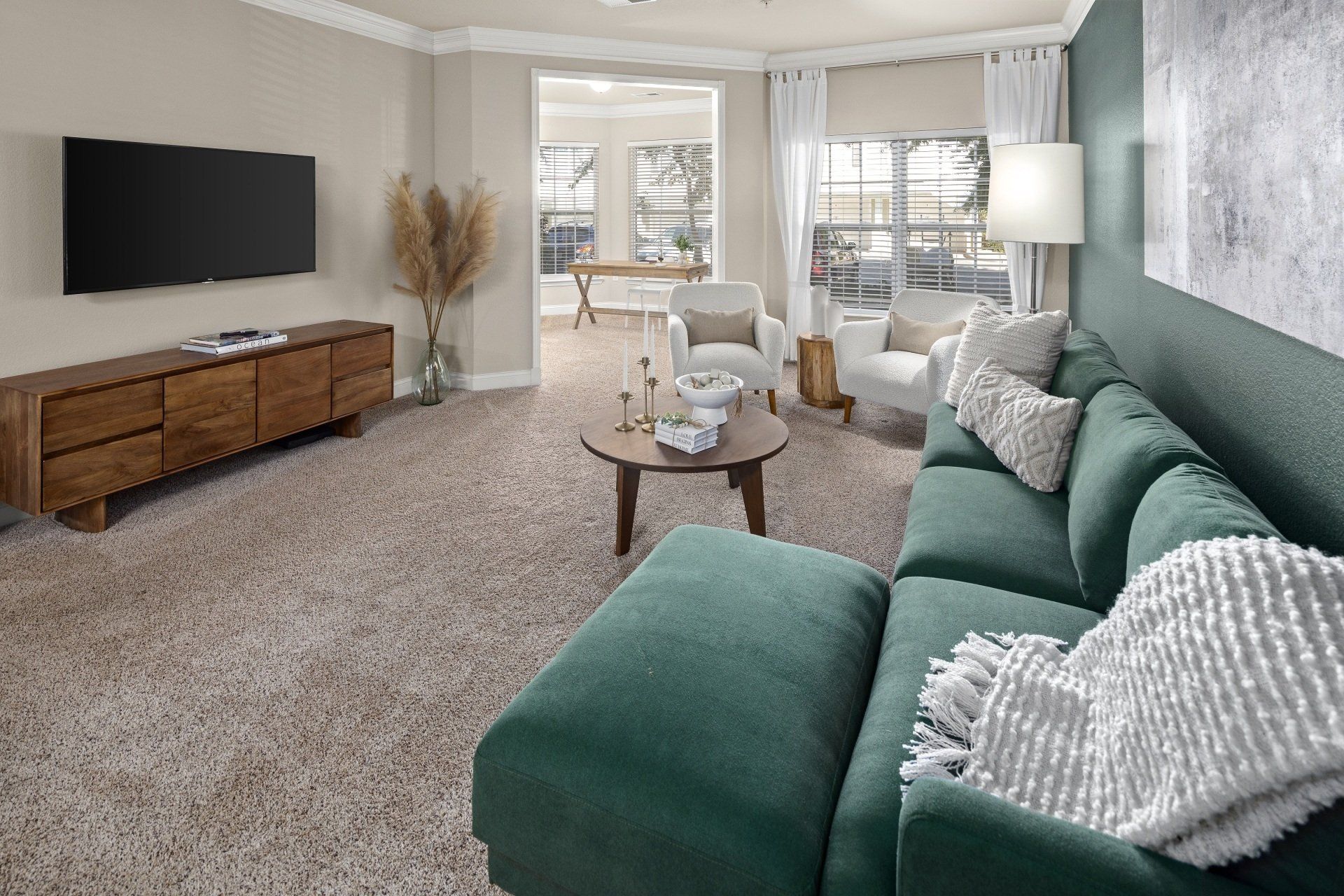 Living room with green sofa, TV, and wooden furniture on beige carpet.