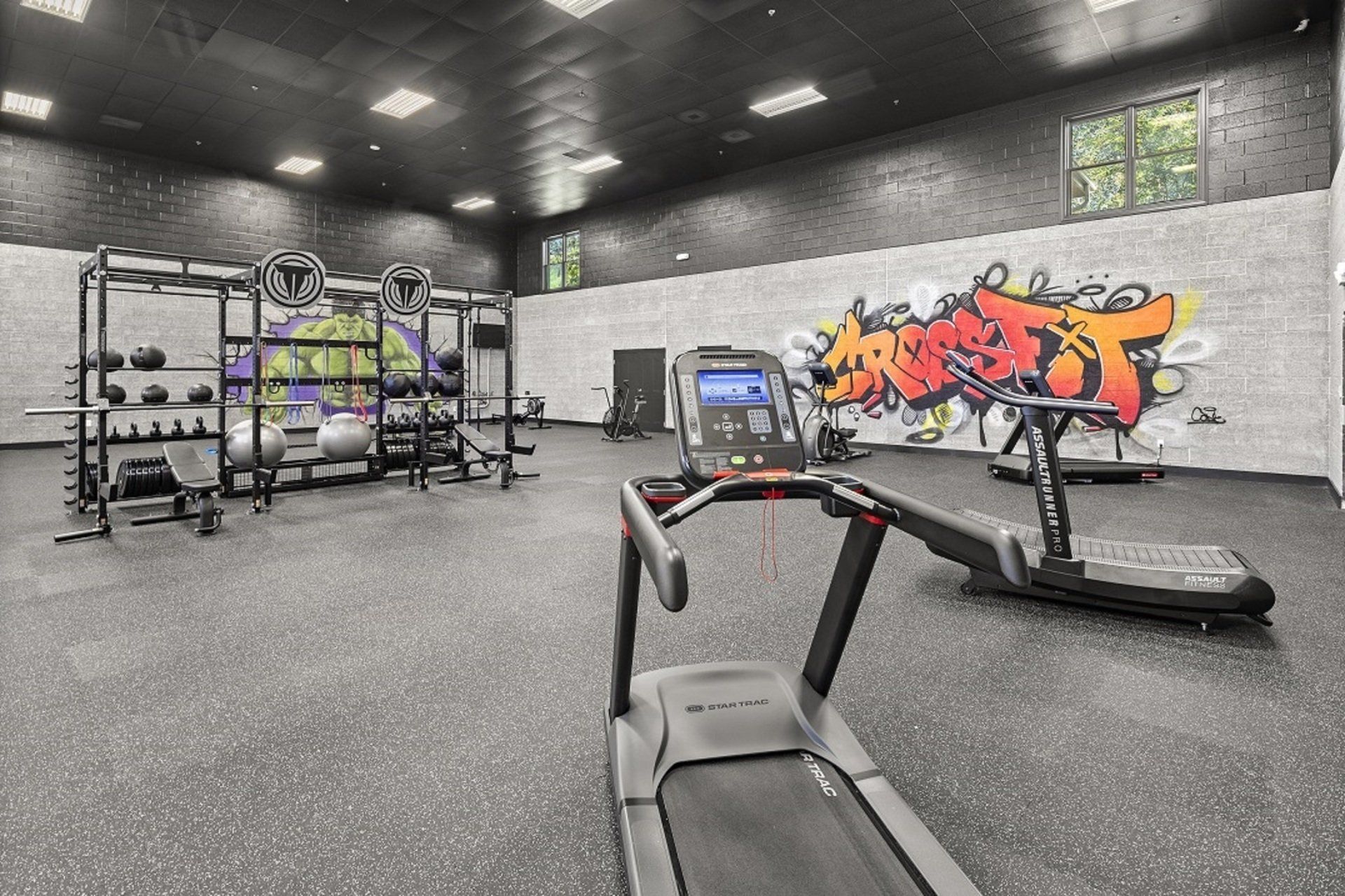 Gym interior with weight racks, treadmills, and graffiti art on the wall.
