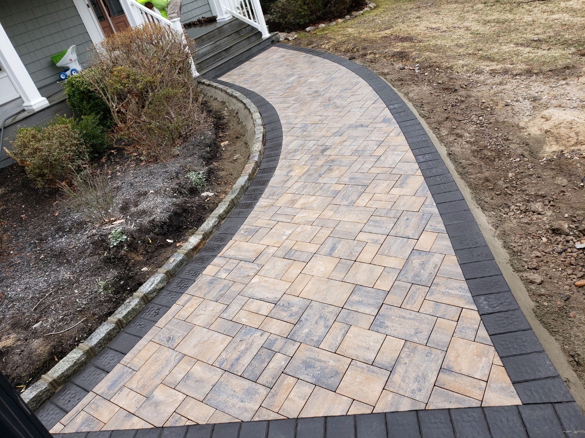 A brick walkway leading to a house with a black border