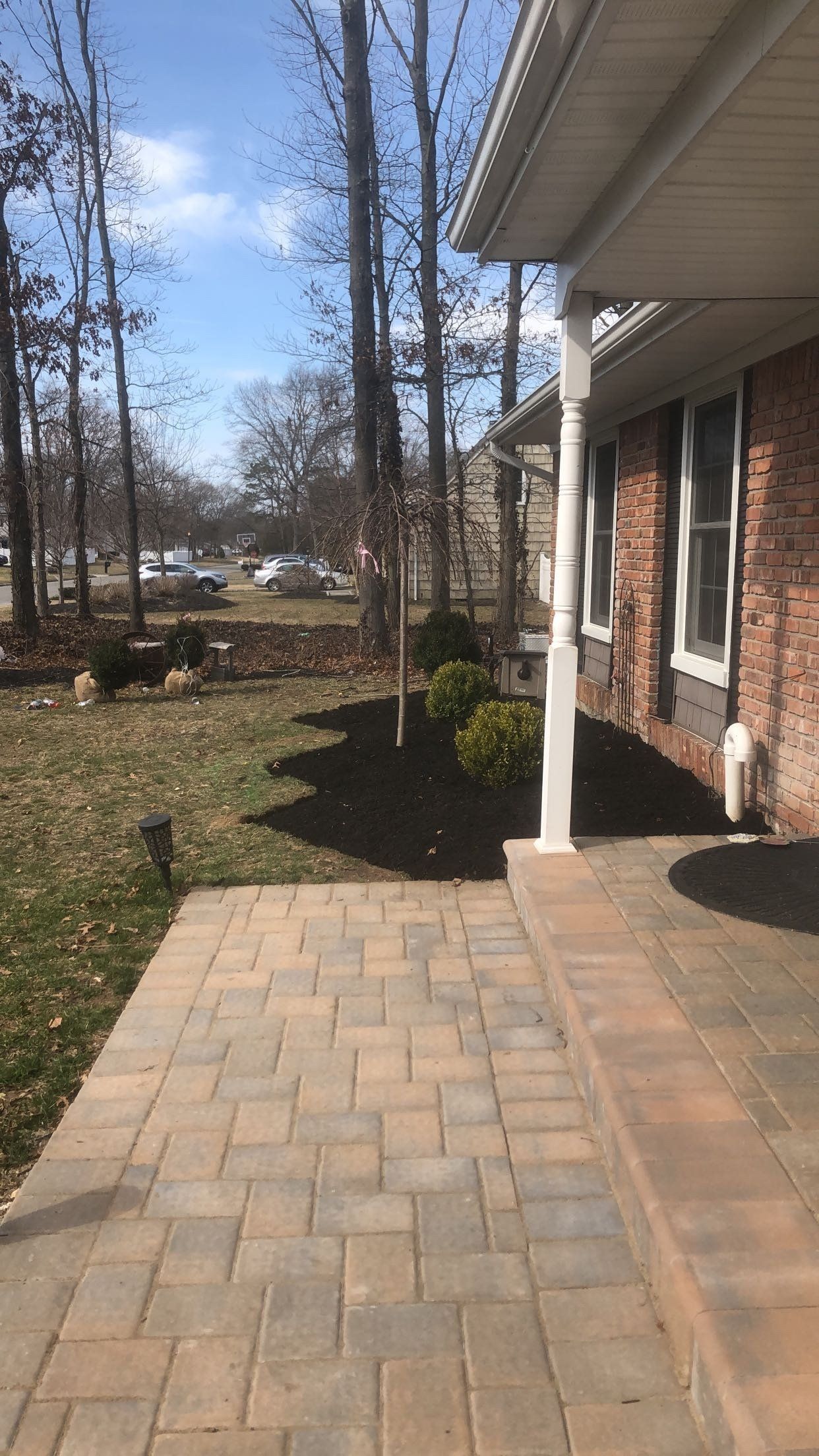 A brick patio in front of a brick house with trees in the background.