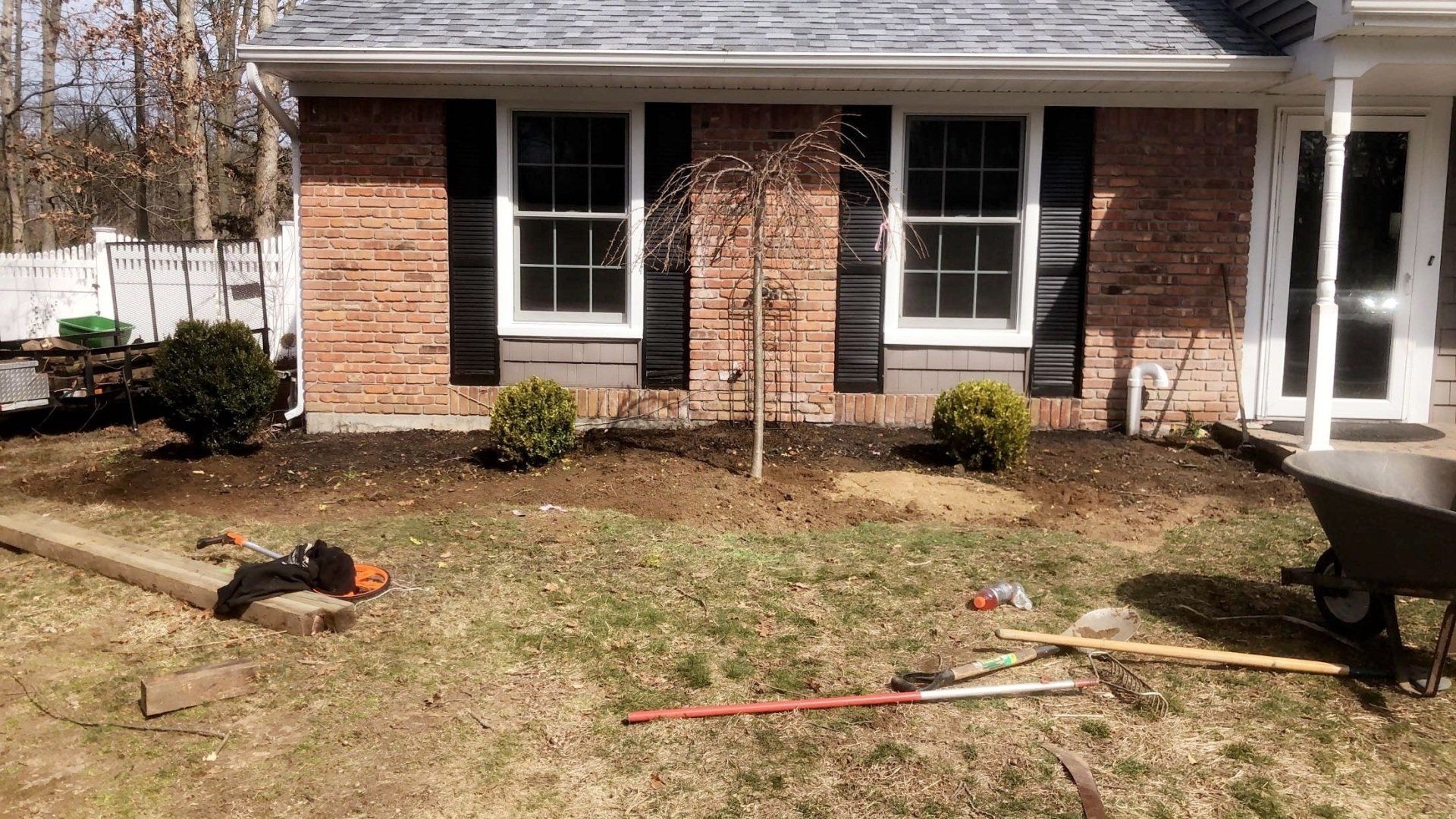 A brick house with black shutters and a wheelbarrow in front of it.