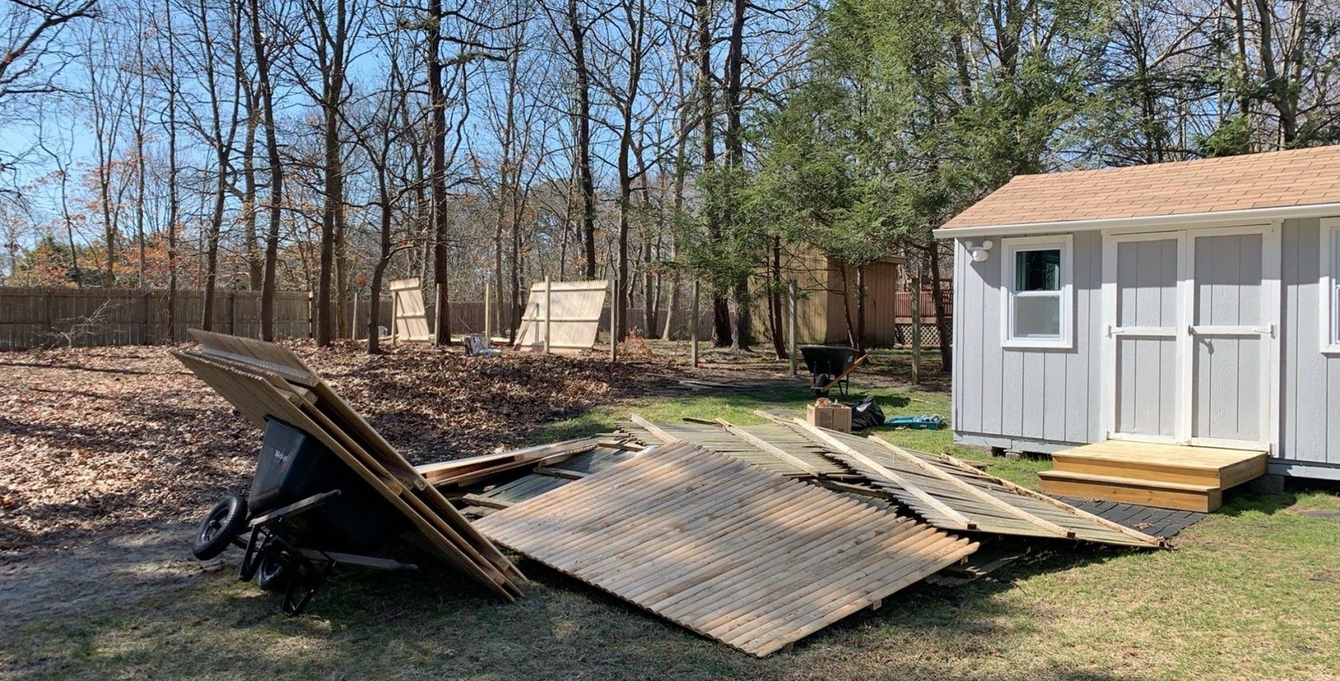 A white shed is sitting in the middle of a yard next to a pile of wood.