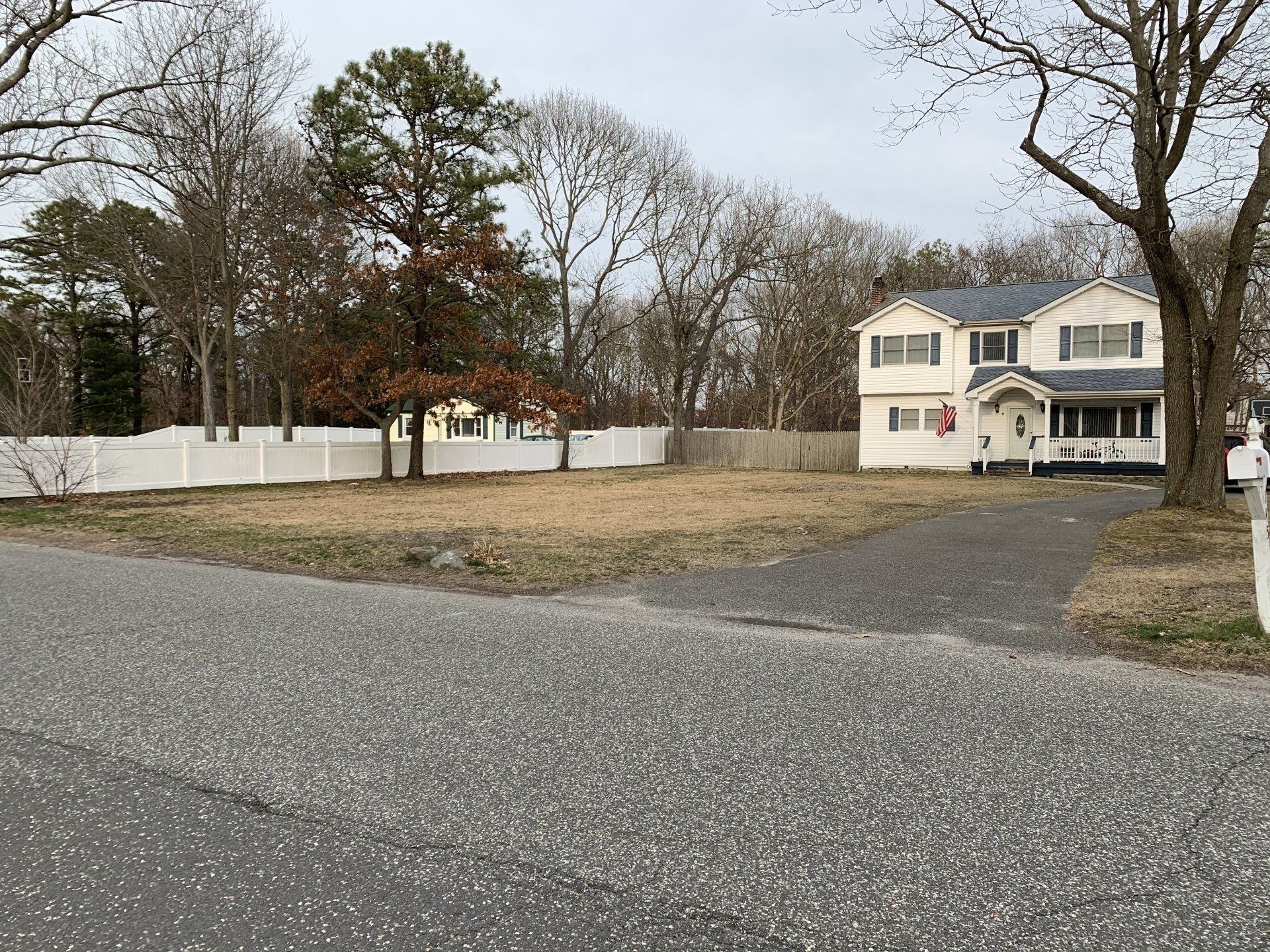 A large white house is sitting on top of a lush green field surrounded by trees.