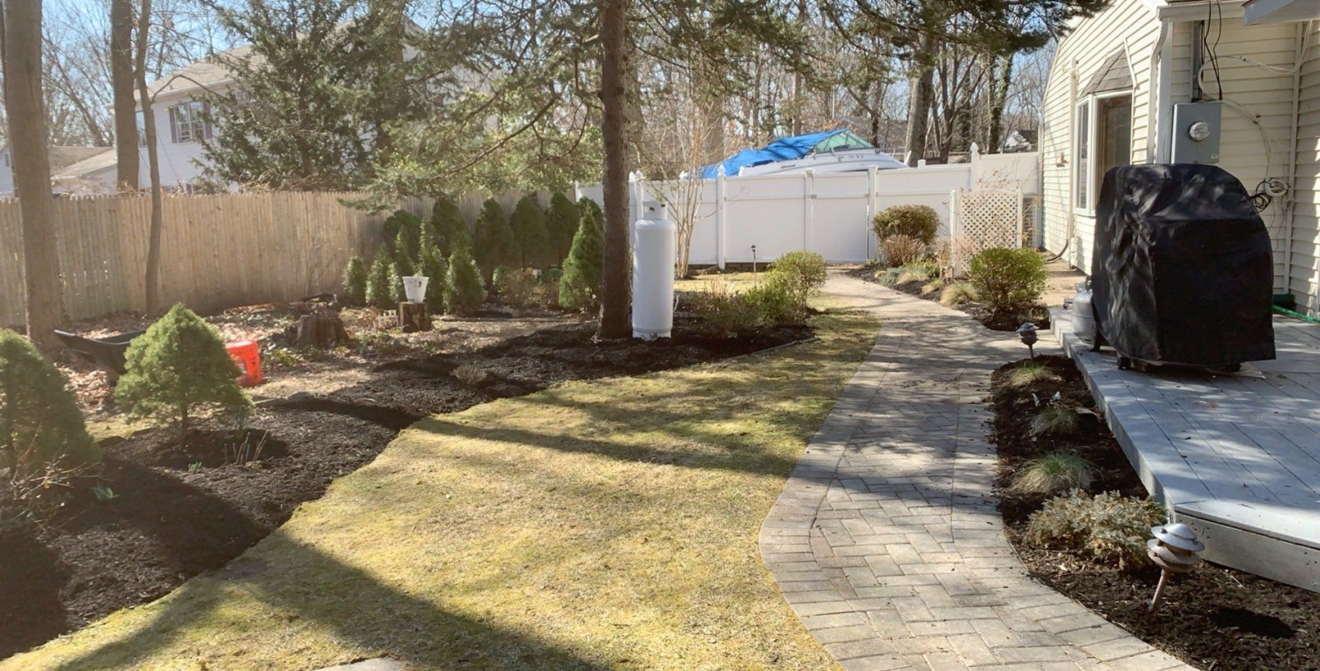 A backyard with a brick walkway leading to a house and a grill.