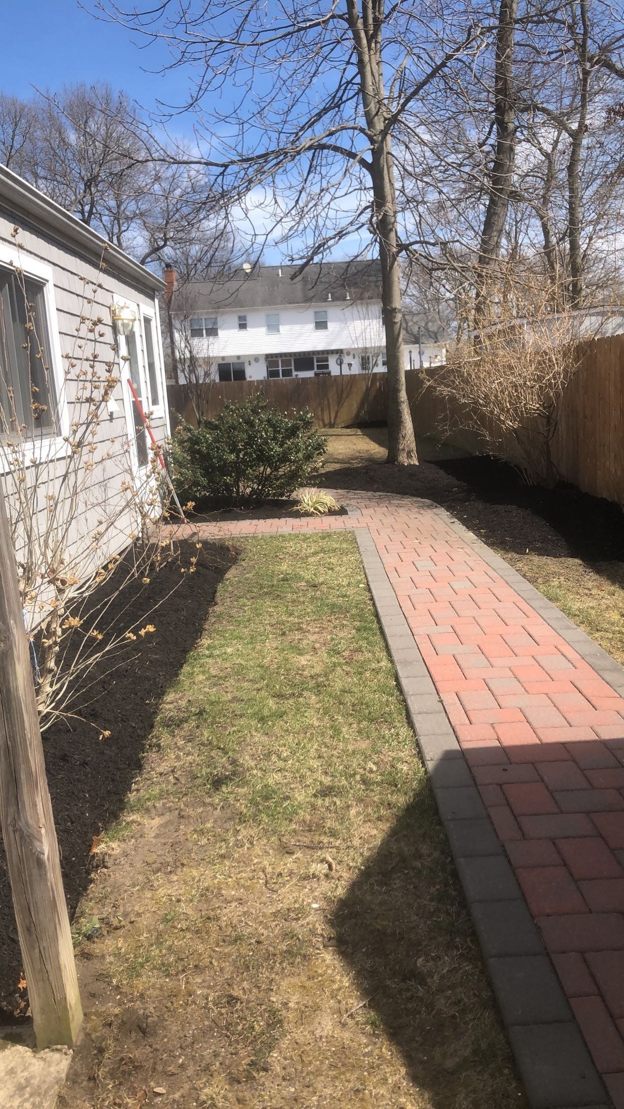 A backyard with a brick walkway leading to a house.
