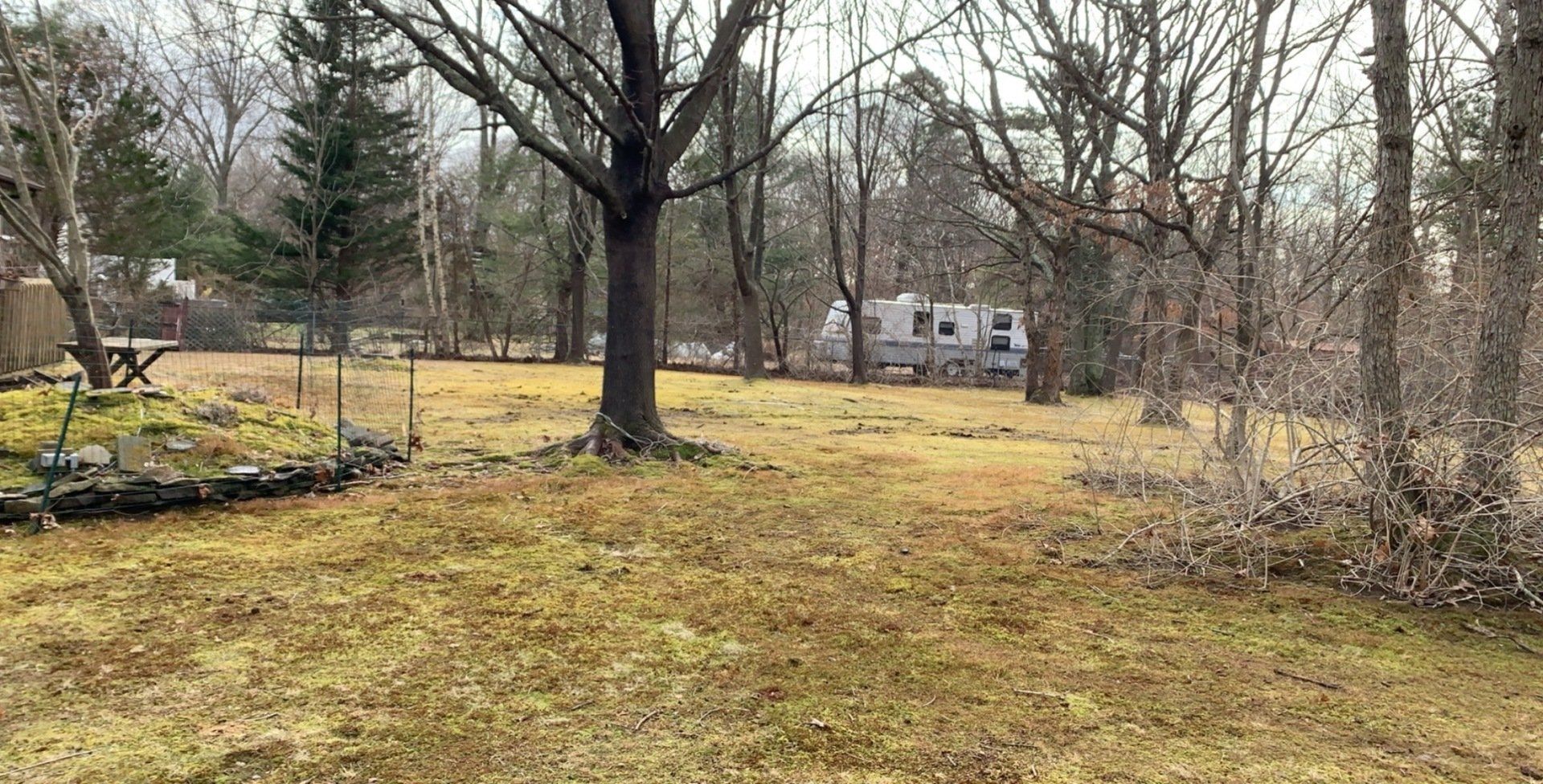 A large grassy field with trees in the background and a house in the background.