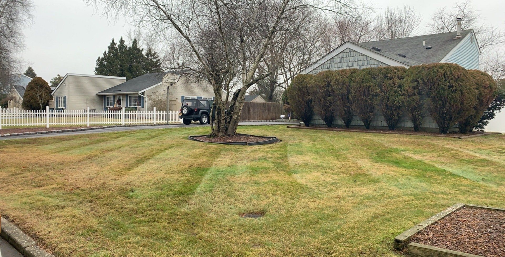 A lawn mower is cutting a lush green lawn in front of a house.